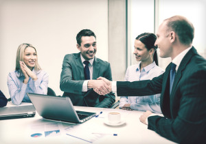 Men shaking hands at table.